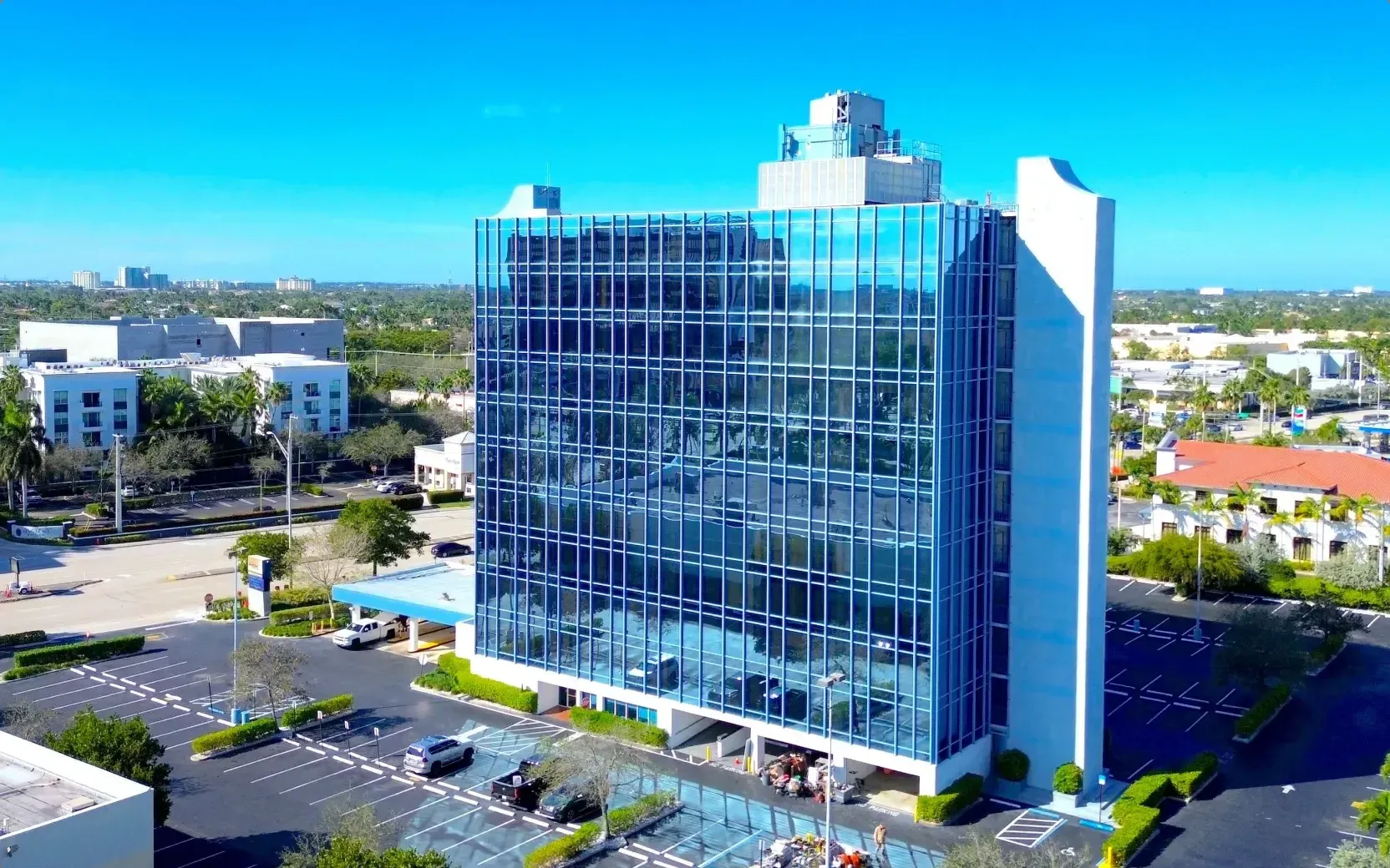 The existing office building seen from the air, standing on its car park among low buildings and planting.